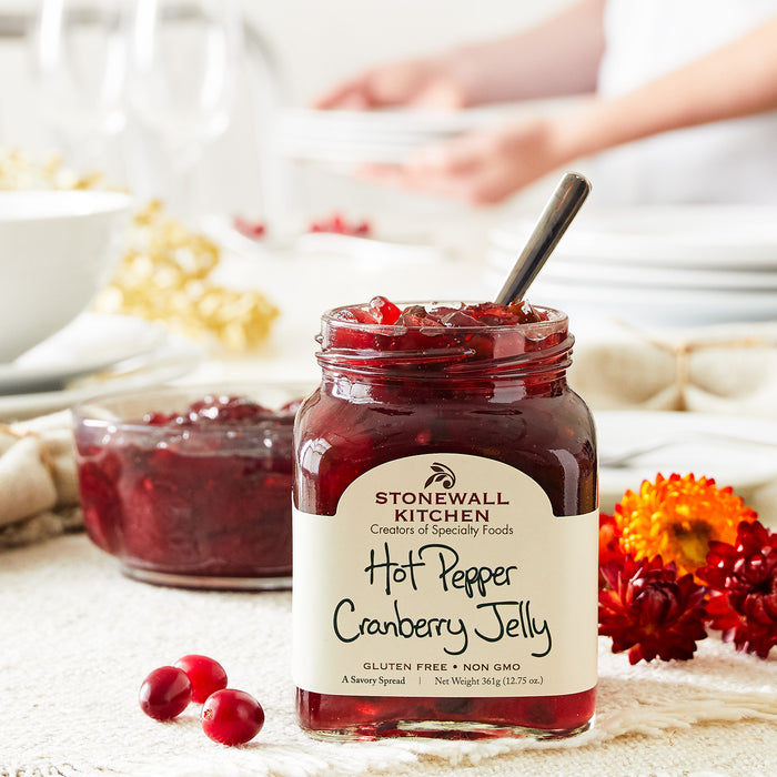 jar of stonewall kitchen hot pepper cranberry jelly with flowers on table and a bowl full of cranberry jelly in the background cranberries in foreground