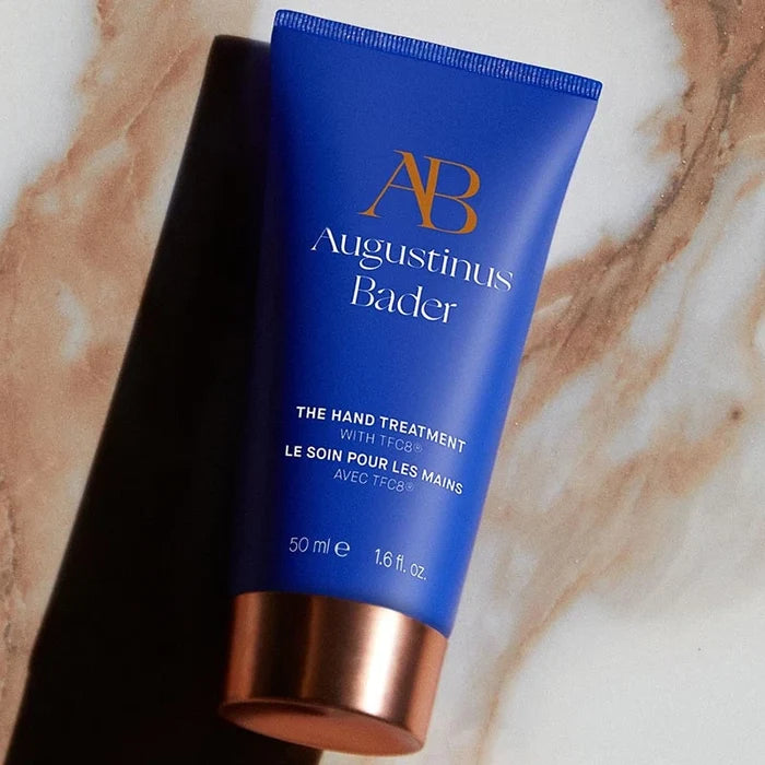 Augustinus Bader The Hand Treatment blue tube with rose-gold cap on marble surface
