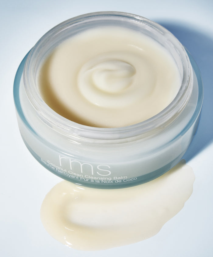 Open jar of Coconut Clean Cleansing Balm showing smooth cream texture with a small amount spread beside the jar on a light surface, highlighting clean beauty and natural ingredients.