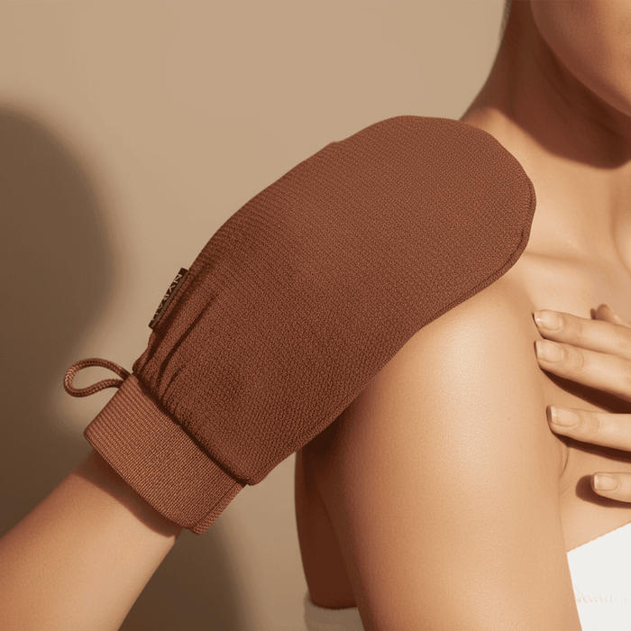 Brown exfoliating glove being used on a person's shoulder against a beige background