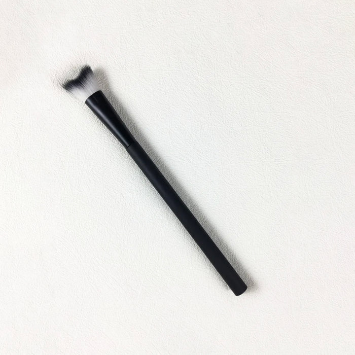 Sleek black makeup brush with angled white and black bristles on textured white background, ideal for precise cosmetic application.
