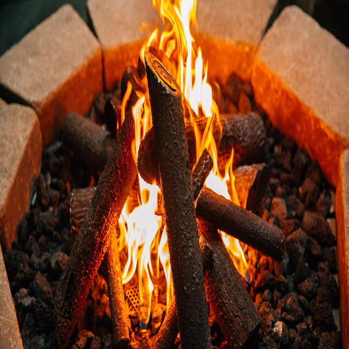 Close-up of Firegear Pro Series brass gas burner flames with realistic ceramic logs and lava rocks in a fire pit setup.