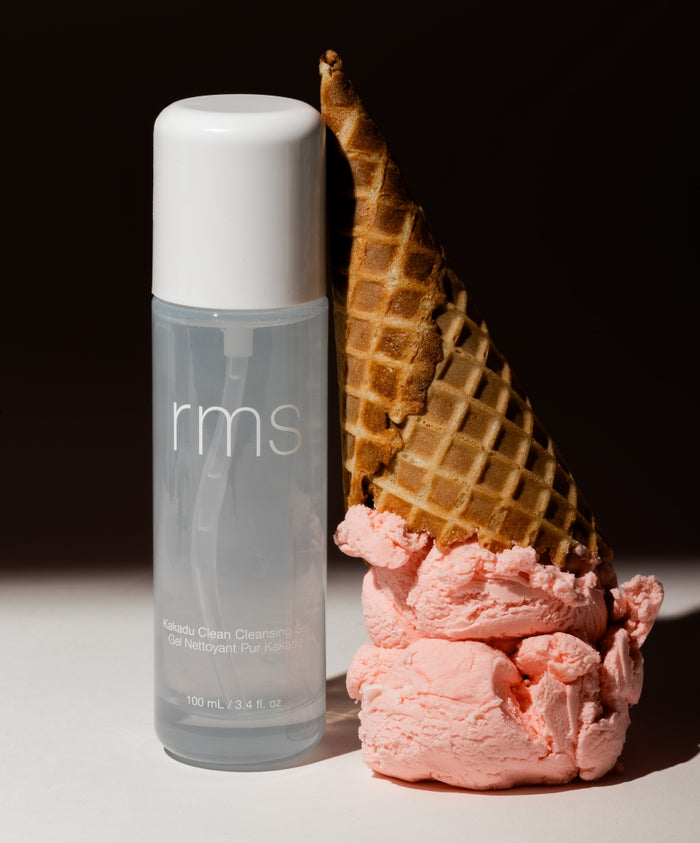 Clear bottle of Kakadu Clean Cleansing Gel with white cap next to a melting waffle cone with pink ice cream on a dark background